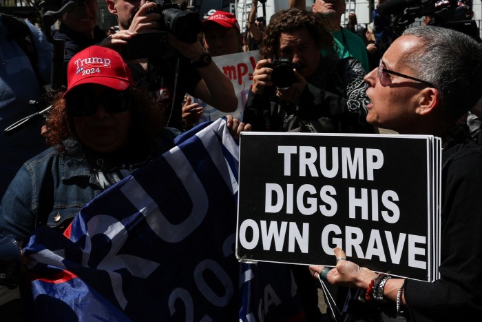 An anti-Trump demonstrator holds a banner next to pro-Trump demonstrators as people gather outside the courthouse in Manhattan