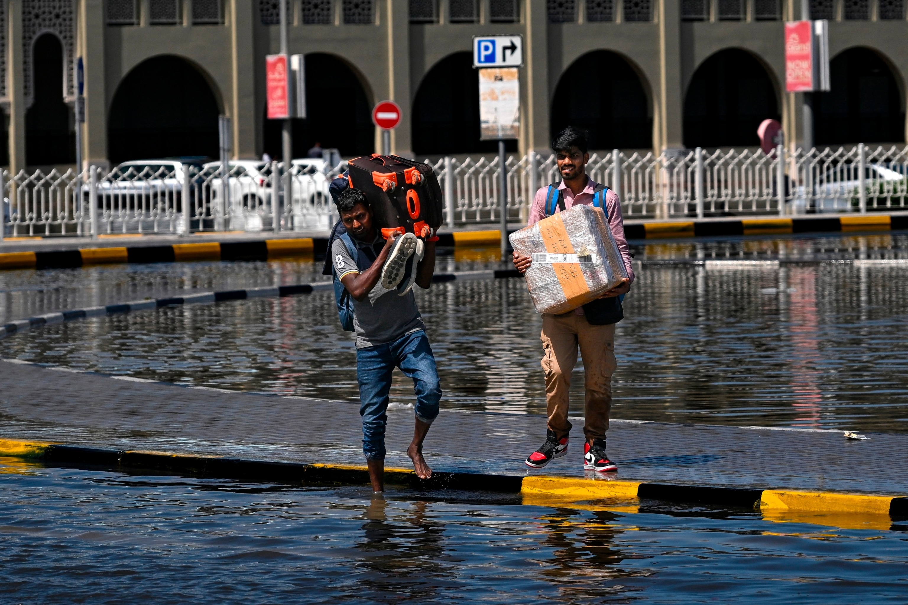 PHOTO: Men prepare to cross a flooded street following heavy rains in Sharjah on April 17, 2024. 