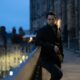 Richard Rankin as John Rebus, wearing a leather jacket and leaning on a wall