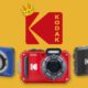 A selection of Kodak cameras, against a yellow background, with the red Kodak logo wearing a miniature crown