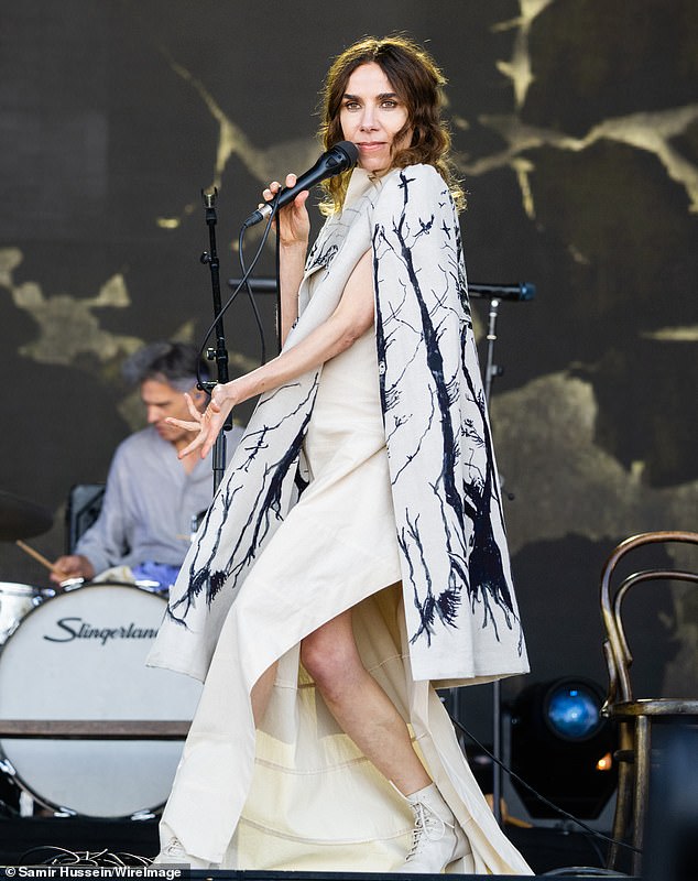 The singer wears a white dress with an intricately designed cape