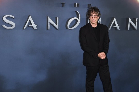 Neil Gaiman standing in front of 'The Sandman' sign at a London premiere