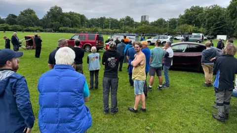 People in a field with hot-air balloon baskets and cars