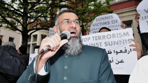 Demotix Choudary campaigning in 2014 - he is holding up a mic and is wearing a green jubba - behind him his supporters hold up signs in support