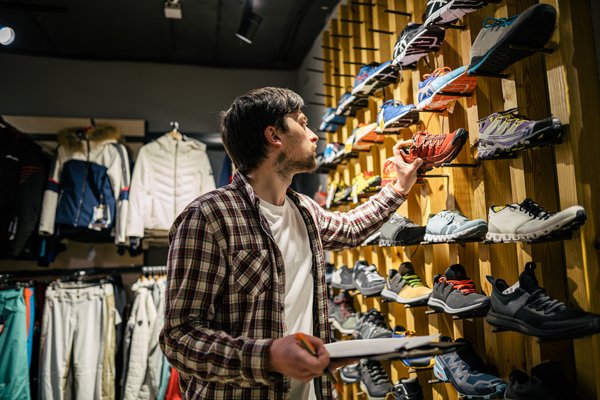 A person with a clipboard doing inventory in a retail shoe store.