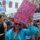 trans pride pic, protester holds placard reading trans healthcare saves lives, illustrating an article about the puberty blocker ban