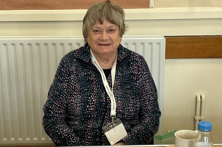 A woman wearing a lanyard sat behind a desk at a polling station