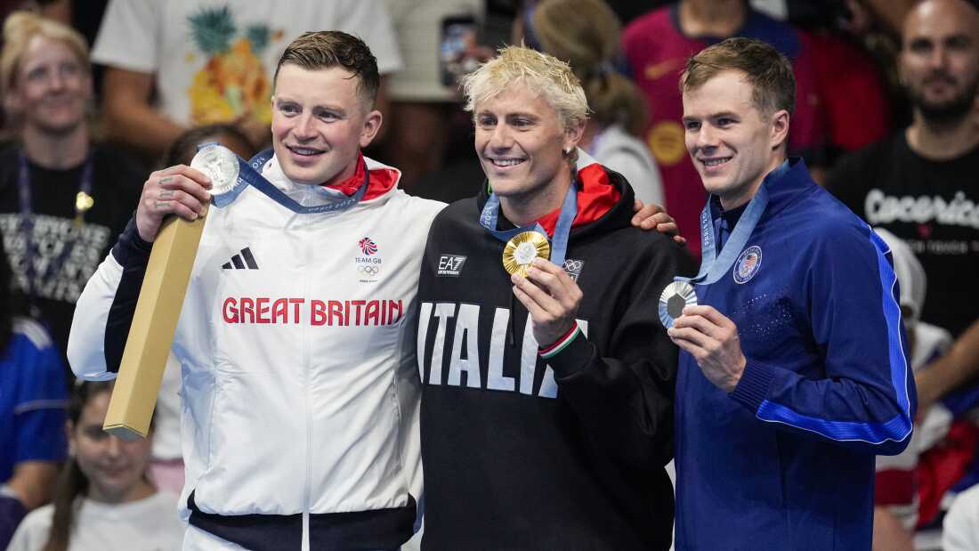 Gold medalist, Nicolo Martinenghi, center, of Italy, stands with silver medalists, Nic Fink, right, of the the United States, and Adam Peaty, of Britain, on the podium after the men's 100-meter breaststroke final at the 2024 Summer Olympics, Sunday, July 28, 2024, in Nanterre, France. (AP Photo/Bernat Armangue)