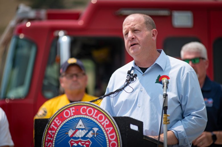 Gov. Jared Polis addresses the audience from a podium labeled 