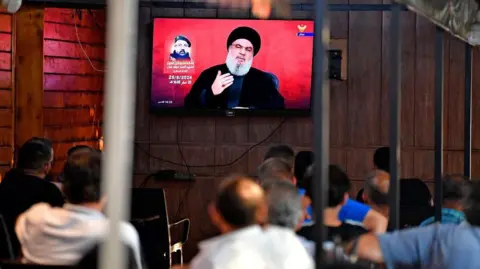 EPA People watch Hezbollah Secretary-General Hassan Nasrallah delivering a televised speech at a coffee shop in the southern suburb of Beirut, Lebanon, 25 August 2024.