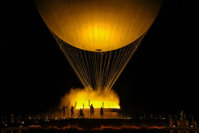 The five final torchbearers lift their torches in front of the cauldron.