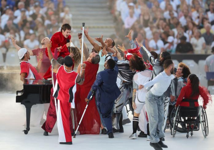 Christine and the Queens stands on a piano and sings, surrounded by dancers, at the Paris 2024 Paralympics Opening Ceremony