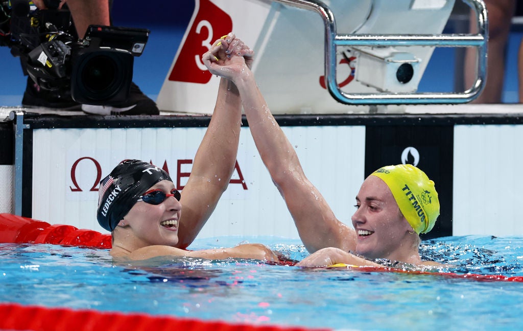 Katie Ledecky has her hand held up in celebration by great rival Ariarne Titmus