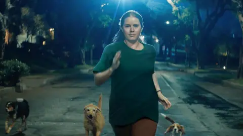 Searchlight Pictures Amy Adams running with a pack of dogs in Nightbitch