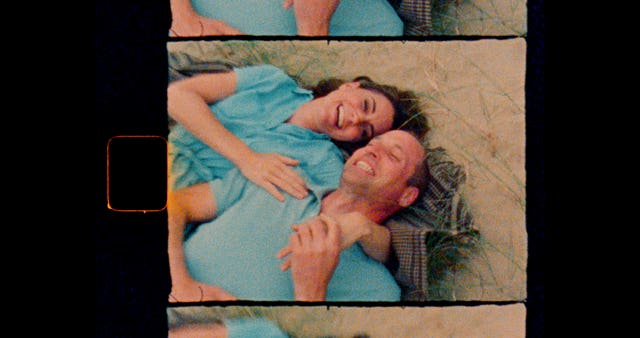 Grainy footage from a video footage shows Kate and William laid on the sand in an embrace, laughing together. The photo has the style of a vintage camera with black sides and heat spot