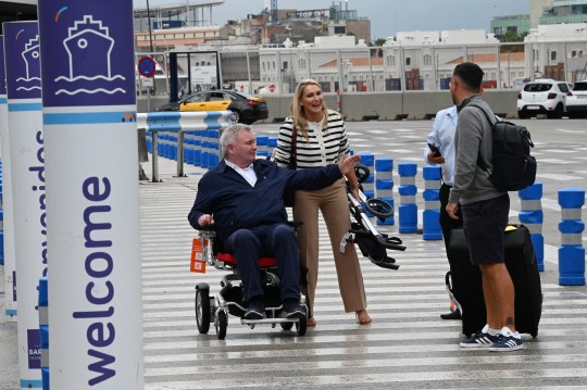 Eamonn Holmes sticking his arm out while in a wheelchair at Barcelona Airpot next to Katie Alexander