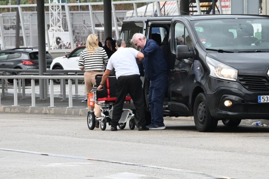 Eamonn Holmes being helped out of a car and into an wheelchair at Barcelona airport 