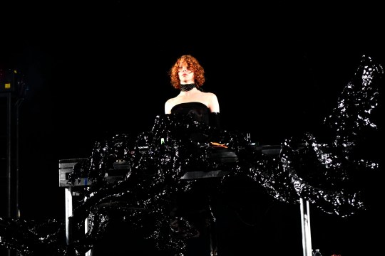 Sophie Xeon performing onstage wearing a trailing black dress over their keyboard