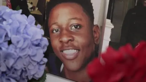 BBC A photo of Malcolm Mide-Madariola with flowers in front of the picture 