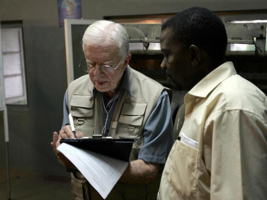 Carter takes notes in December 2004 while listening to a translator during a polling station observation visit in Maputo, Mozambique. The Carter Center says it has monitored 125 elections in 40 countries as of August 2024.