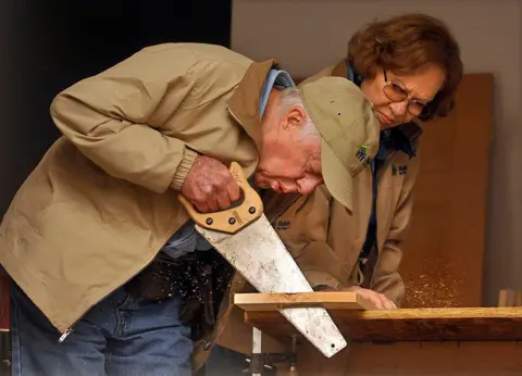 Getty Images Carter and Rosalynn Carter cut a piece of wood with a saw