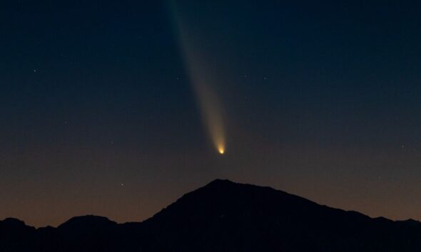 a fuzzy bright orb leaves a trail behind it in the night sky above the silhouette of a mountain