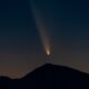 a fuzzy bright orb leaves a trail behind it in the night sky above the silhouette of a mountain