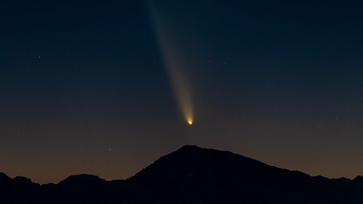 a fuzzy bright orb leaves a trail behind it in the night sky above the silhouette of a mountain