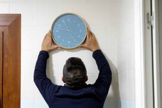 Rear view of man fixing a blue clock on a white wall