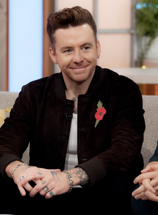 Danny Jones smiling on Lorraine, wearing a black jacket with a red poppy attached and a white top 