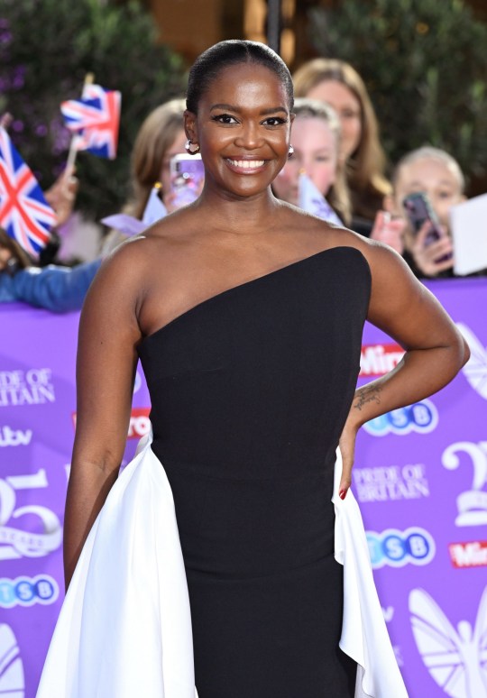 Oti Mabuse smiling on the red carpet in a strapless black and white dress, with her hand on her hip