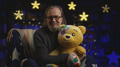 Gary Oldman holding a Pudsey the bear with stars in the background