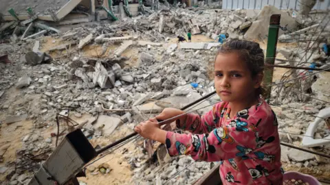 Getty Images A girl stands among the rubble of buildings destroyed by Israeli air strikes in in Khan Yunis, the Gaza Strip. Photo: 17 November 2024