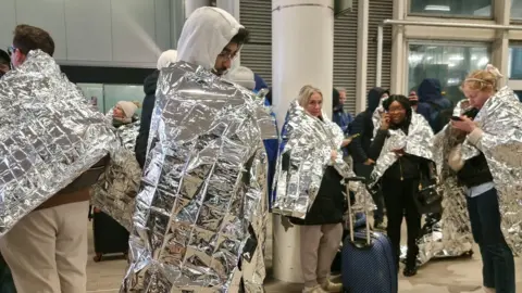 Marco Pajo Passengers at Gatwick Airport after an evacuation. They are covered in silver foil heat warmers. 