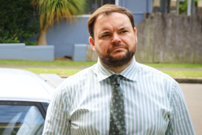 Lloyd Griffith plays Colin Cartwright, stood outside wearing a shirt and tie