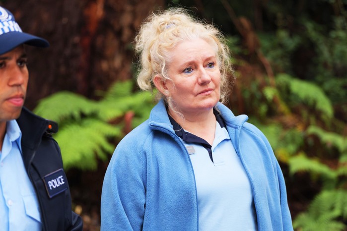 Celia Ireland as Reggie Rocco, standing outside, wearing a blue top and jacket