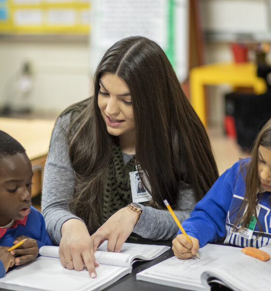 An education student helps two elementary students in their classroom.