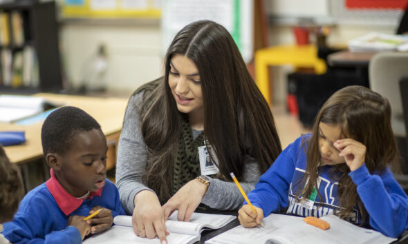 An education student helps two elementary students in their classroom.