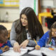 An education student helps two elementary students in their classroom.