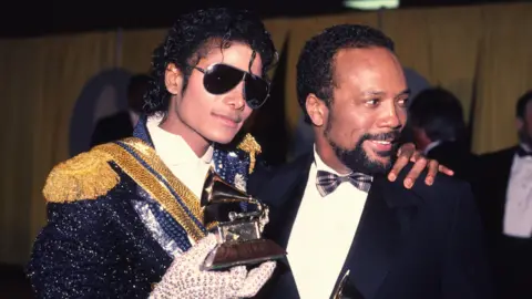 Getty Images Michael Jackson (left) and Quincy Jones at the Grammys - Jackson is wearing a sequinned jacket and his trademark single white glove. Jones is wearing a tux with a tartan bow tie.