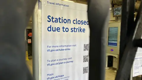 BBC Shutters closed at Kentish Town Station during a Rail and Tube Strike. There is a poster behind the closed barrier saying 'Station closed due to strike'.