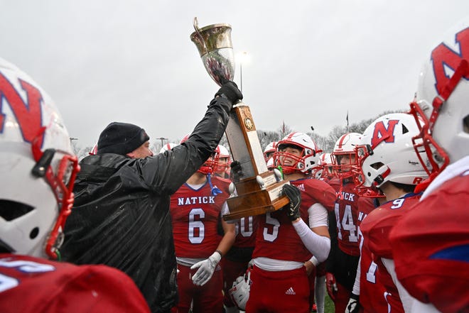 Natick head coach Mark Mortarelli hands the Elks trophy to senior James Perrier after defeating Framingham, 42-15, during the annual Thanksgiving Day football game at Memorial Field in Natick, Thursday, Nov. 28, 2024.