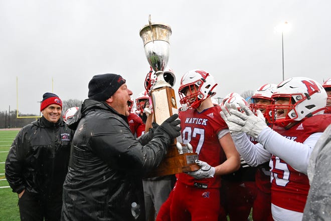 Natick head coach Mark Mortarelli hands the Elks trophy to senior Simon Pedrelli after defeating Framingham, 42-15, during the annual Thanksgiving Day football game at Memorial Field in Natick, Thursday, Nov. 28, 2024.