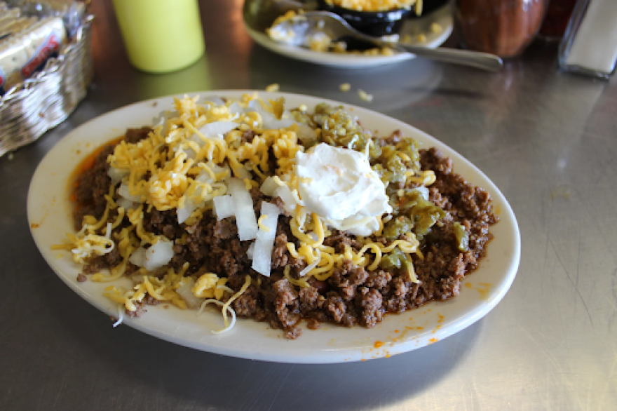 Plate of Dixon's Famous Chili on a metal table top, topped with onions, cheese, and sour cream.