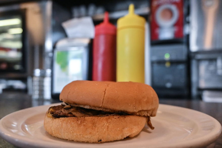 A burger from Town Topic on a white plate with ketchup and mustard containers in the background.