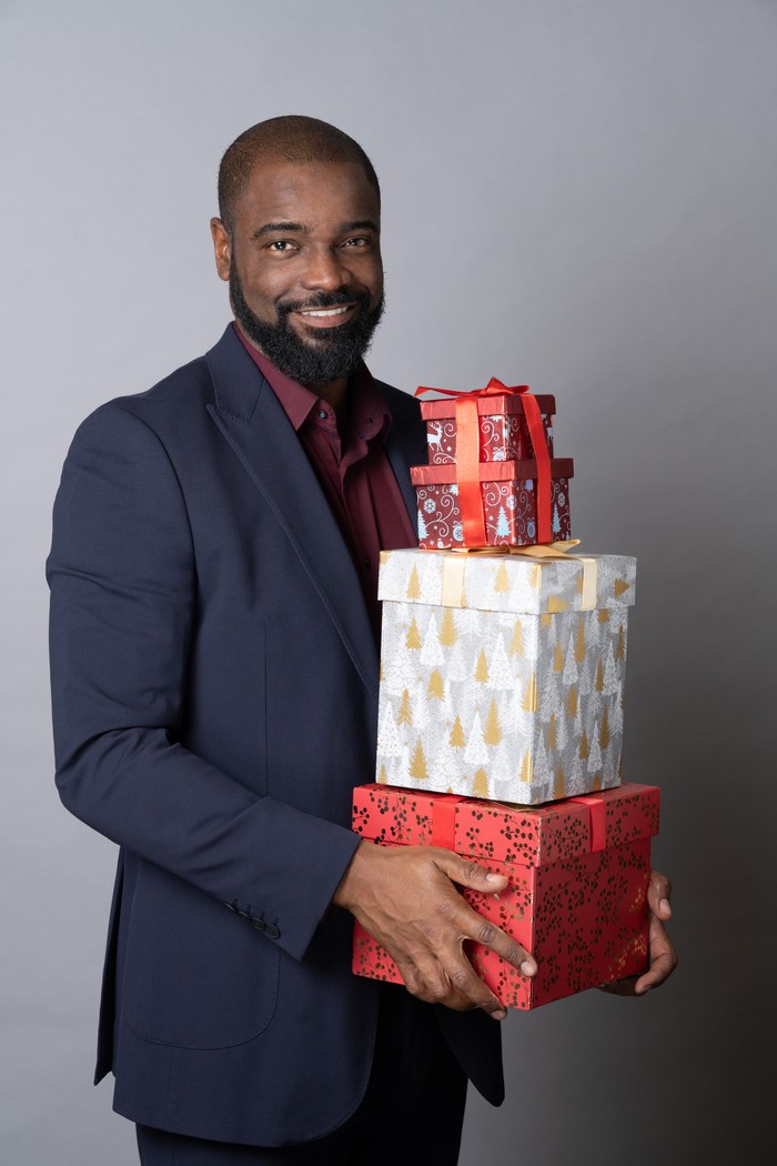 Micah Balfour smiles and poses with presents as Junior Knight in a Christmas photoshoot for EastEnders.