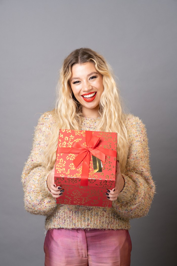 Molly Rainford smiles and poses with a Christmas present as Anna Knight in a photoshoot for EastEnders at Christmas.