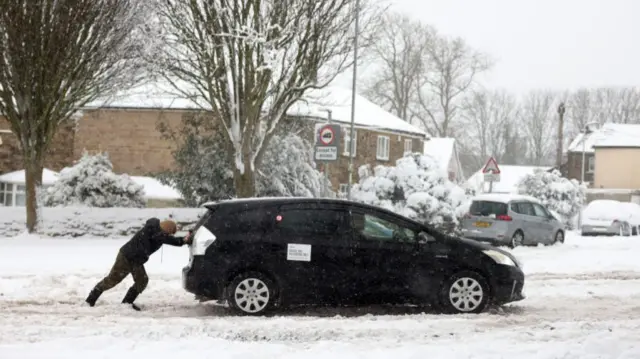 A person helps push a stranded car on January 05, 2025 in Bradford