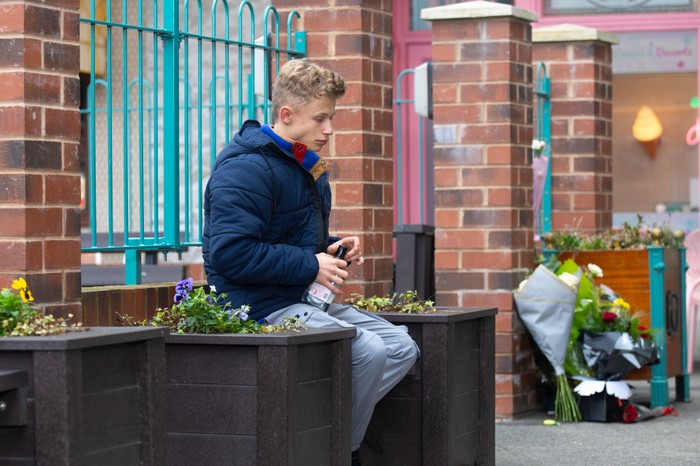 Dylan sitting outside with a bottle in Coronation Street