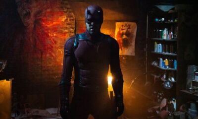 Charlie Cox in full Daredevil outfit in a dimly lit room with exposed brick wall